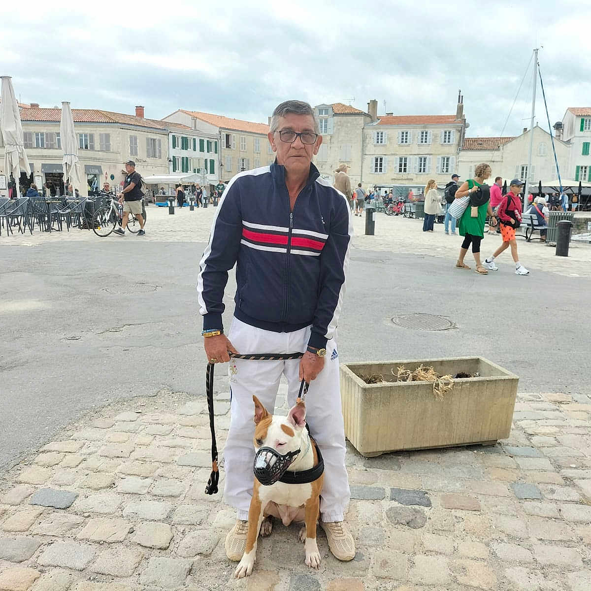 Spajk participe au concours pour gagner de l'argent avec cette photo : man, dog, leash, muzzle, street, cobblestone, people, buildings, outdoor, cloudy_sky, casual_clothing, glasses, plant_pot, walking, urban, sidewalk, public_space, daytime, pedestrians, bicycle