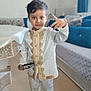 Ziyad a rejoint le concours — aidez-le/la à gagner de superbes lots ! child, boy, toy_car, white_clothing, gold_trim, standing, indoor, carpet, couch, pillows, furniture, hand_gesture, portrait, smiling, short_hair, socks, home_interior, radiator, curtains, carpeted_floor
