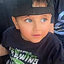 toddler, child, boy, cap, black_cap, black_shirt, graphic_tshirt, curious, bright_eyes, portrait, indoor, casual_clothing, cute, young_child, human, sitting, face, headwear, expression, light