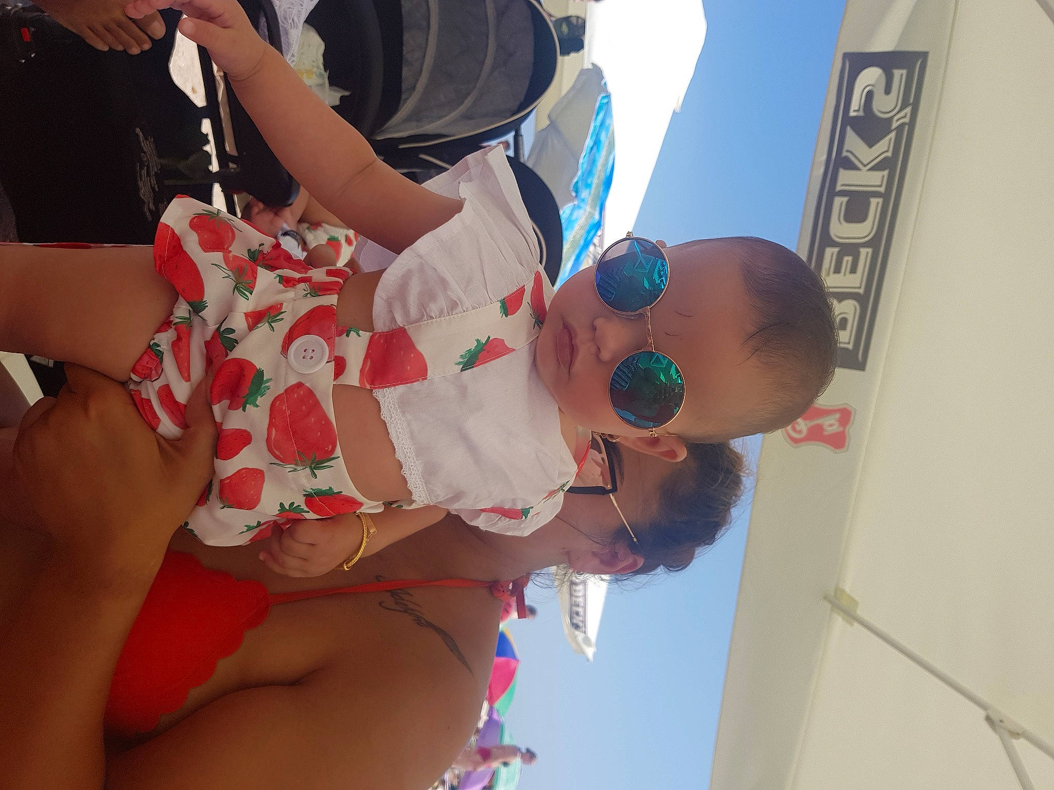 Zeny is registered to the contest to win money with this photo: child, elbow, event, eyewear, friendship, fun, gesture, goggles, happy, hat, human_leg, leisure, people_on_beach, person, recreation, shorts, sky, sunglasses, thigh, toddler