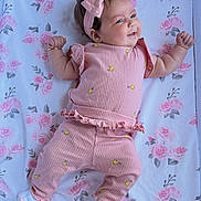 Rosemary is registered to the contest to win money with this photo: baby, infant, pink_outfit, headband, bow, smile, lying_down, blanket, floral_pattern, cute, child, soft_lighting, indoors, happy, adorable, person, small_hands, cozy, playful, toddler