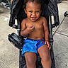Casimir is registered to the contest to win money with this photo: toddler, child, smiling, stroller, outdoor, playground, pacifier, fan, blue_shorts, blue_boots, curly_hair, sitting, portrait, happy, baby, family_outing, concrete, wheelchair, park, daylight