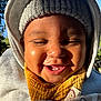baby, smiling, face, hat, knitted_hat, bib, yellow_bib, blanket, patterned_blanket, outdoor, sunlight, happy, closeup, child, headwear, warm_clothing, nature, blue_sky, person, cute
