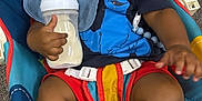 Casimir is registered to the contest to win money with this photo: baby, smiling, bottle, milk, baby_chair, fisher_price, clothing, socks, happy, child, indoor, colorful, bib, toddler, person, seatbelt, toy, furniture, face, cute