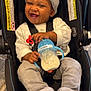 baby, car_seat, smiling, hat, sippy_cup, milk, clothing, child, infant, seatbelt, happy, person, cute, toddler, indoor, gray_hat, casimir, baby_toy, socks, jeans