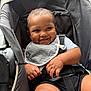 baby, smiling, stroller, child, infant, bib, straps, happy, cute, portrait, seated, hands, clothing, black_shorts, closeup, skin, person, baby_chair, baby_boy, comfort