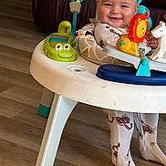 Bodie is registered to the contest to win money with this photo: baby, child, smiling, walker, toy, indoor, floor, pajamas, playful, crocodile_toy, lion_toy, person, furniture, couch, wooden_floor, happy, cute, legs, face, infant