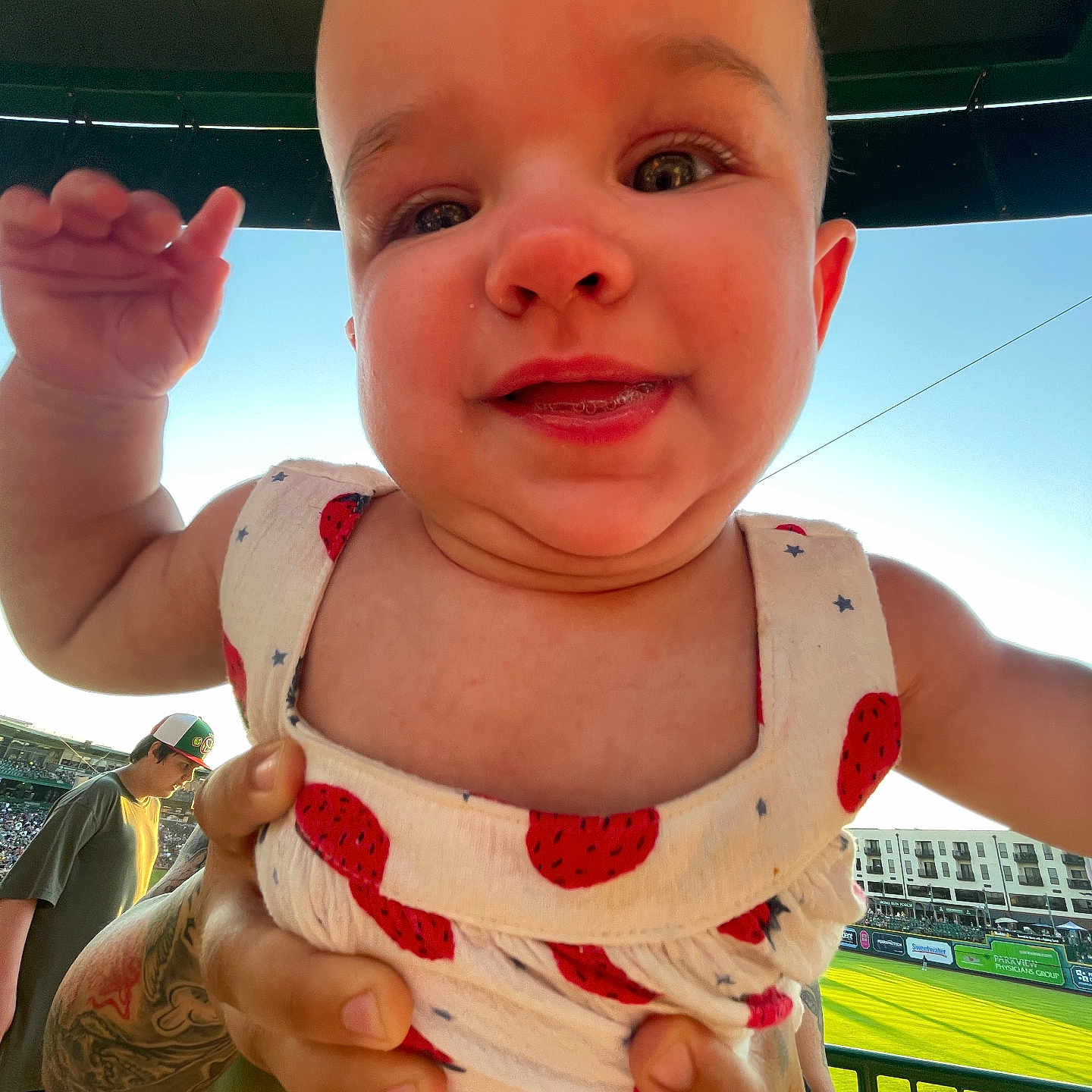 Winona joined the competition — help win amazing prizes! baby, child, daytime, dress, face, fence, field, grass, hand, happy, hat, outdoor, pattern, people, person, smile, spectator, stadium, sunlight, tattoo