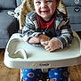 baby, child, colorful_clothing, couch, cozy, cute, face, floor, furniture, happy, high_chair, indoor, living_room, pajamas, person, plaid_jacket, seated, smiling, toddler, wooden_wall