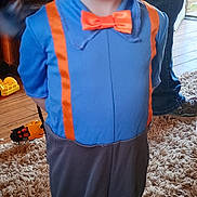 Perry is registered to the contest to win money with this photo: child, costume, orange_hat, orange_glasses, orange_bow_tie, orange_suspender, blue_shirt, gray_pants, barefoot, smiling, indoor, carpet, toy, water_bottle, person, pants, feet, happy, glasses, floor