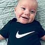 Urijah joined the competition — help win amazing prizes! baby, smiling, black_shirt, nike_logo, drool, blue_quilt, happy, face, infant, cute, clothing, person, portrait, lying_down, skin, head, eyes, mouth, expression, indoors