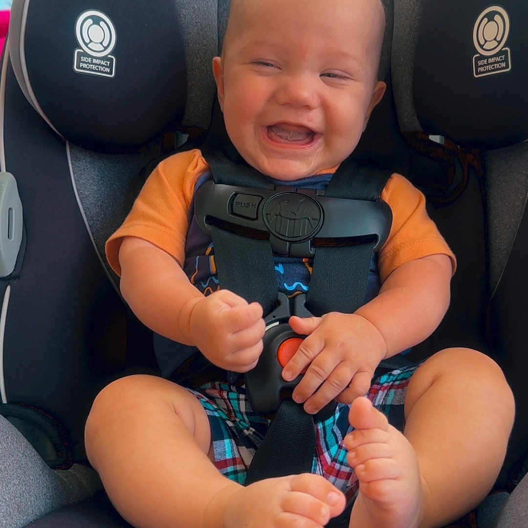 Urijah joined the competition — help win amazing prizes! baby, barefoot, car_seat, child, child_safety, clothing, face, feet, hands, happy, head, indoors, infant, orange_shirt, plaid_shorts, protection, safety, seat, seatbelt, smiling