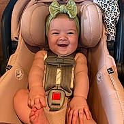 Stevie is registered to the contest to win money with this photo: baby, infant, car_seat, smile, headband, green_bow, blanket, leopard_print, happy, child, seatbelt, cute, skin, hand, foot, indoors, person, toddler, sitting, portrait