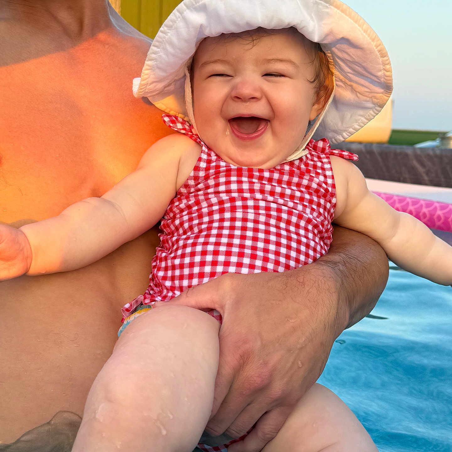 Stevie is registered to the contest to win money with this photo: adult_hand, arm, baby, checkered_pattern, child, fun, happy, laughing, leg, outdoor, pool, skin, smiling, summer, sun_hat, sunlight, swimsuit, vacation, warm_light, water