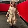 Della is registered to the contest to win money with this photo: child, girl, smile, blonde_hair, dress, floral_pattern, indoor, carpet, wall, red_wall, black_wall, lighting, portrait, standing, happy, floor, room, hair, person, cute