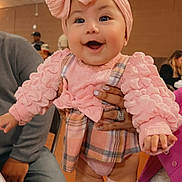 Stormi joined the competition — help win amazing prizes! baby, child, pink_clothing, headband, smiling, indoor, person, hands, adult, plaid_skirt, socks, cute, happy, infant, fashion, portrait, family, celebration, people, seated