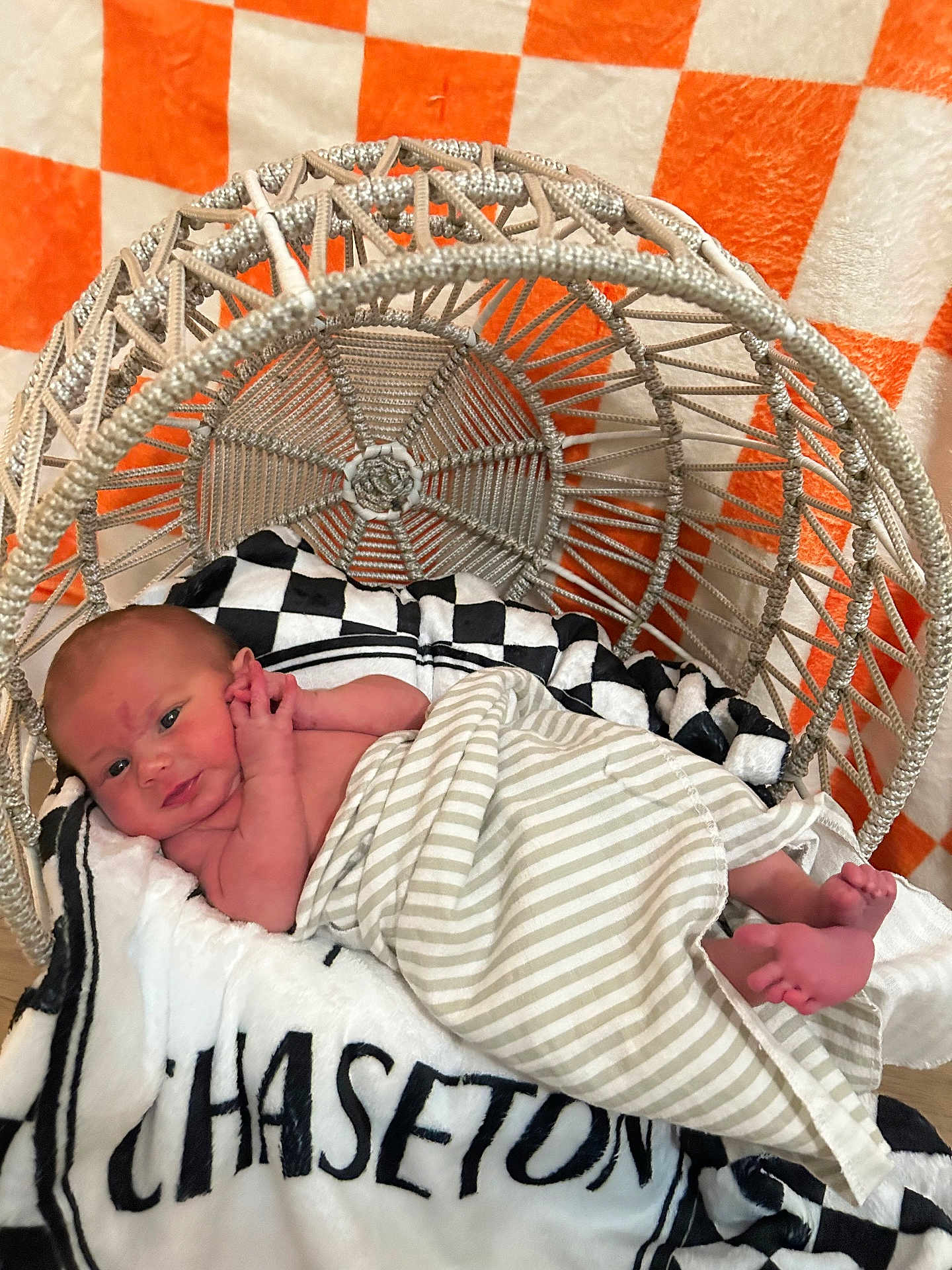 Chaseton is registered to the contest to win money with this photo: baby, basket, black, blanket, checkered_background, comfort, cozy, face, feet, hand, indoor, infant, lying_down, newborn, orange, soft_texture, striped_blanket, white, woven_chair, wrapped