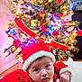 Ailany is registered to the contest to win money with this photo: baby, christmas_tree, holiday, red_clothing, santa_hat, festive, decorations, lights, indoor, cute, child, infant, holiday_season, celebration, cozy, face, portrait, smiling, seasonal, christmas