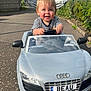 Beau joined the competition — help win amazing prizes! child, toddler, toy_car, audi, smiling, outdoor, road, pavement, greenery, daylight, happy, person, vehicle, license_plate, clothing, short_hair, small_car, play, fun, cute