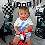 Beau is registered to the contest to win money with this photo: toddler, child, birthday, toy, scooter, balloon, banner, celebration, indoor, happy, cute, smile, red, blue, white, black, party, floor, clothing, face