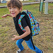 Milo is registered to the contest to win money with this photo: backpack, black_shirt, boy, casual_clothing, child, daylight, field, fun, grass, hair, jeans, nature, outdoor, playful, pose, sky, smile, sneakers, sunset, young