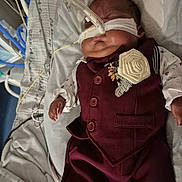 Mateo Marcelin is registered to the contest to win money with this photo: baby, infant, hospital, medical_tubes, nasogastric_tube, maroon_suit, boutonniere, sleeping, bed, blanket, medical_equipment, newborn, child, patient, clothing, face, portrait, healthcare, resting, indoors