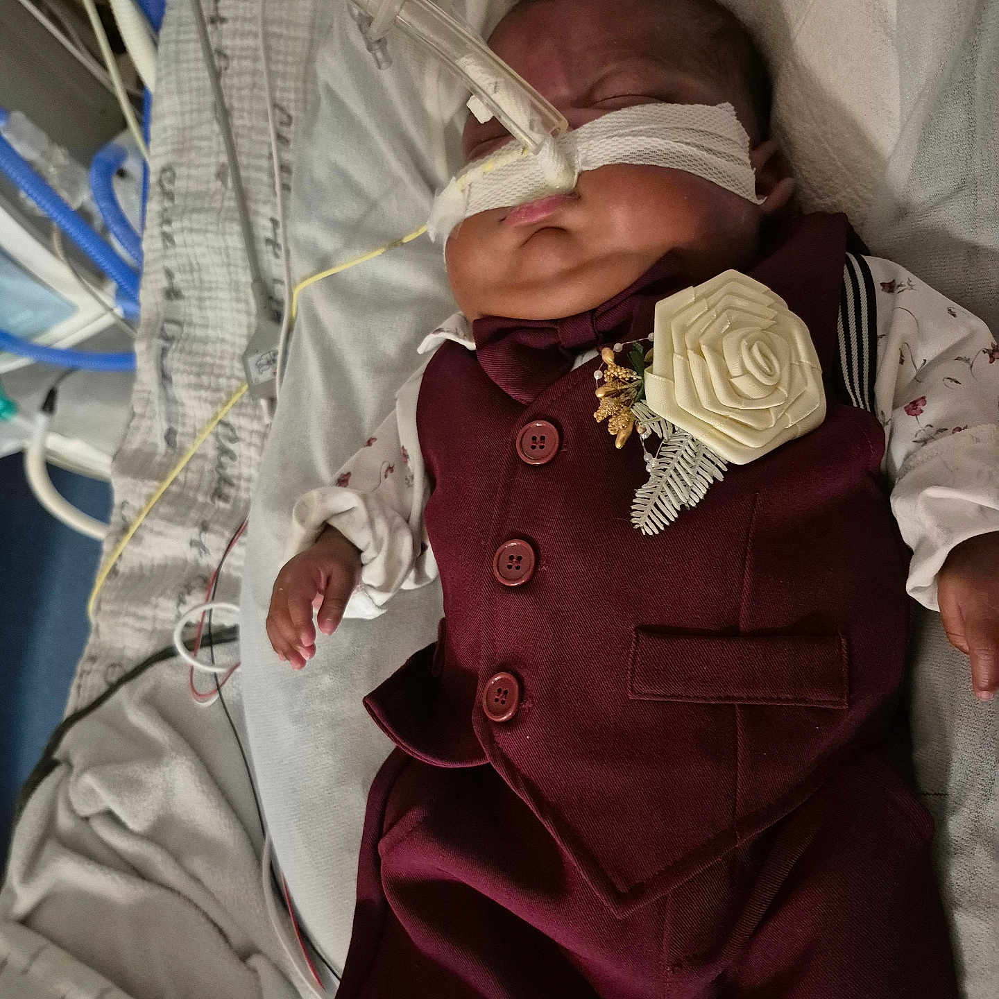 Mateo Marcelin is registered to the contest to win money with this photo: baby, bed, blanket, boutonniere, child, clothing, face, healthcare, hospital, indoors, infant, maroon_suit, medical_equipment, medical_tubes, nasogastric_tube, newborn, patient, portrait, resting, sleeping