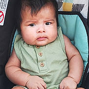 Darkiel joined the competition — help win amazing prizes! baby, child, infant, green_outfit, sleeveless, wooden_buttons, baby_seat, patterned_background, chubby_cheeks, curly_hair, serious_expression, barefoot, hands, legs, indoor, portrait, close_up, seatbelt, car_seat, person