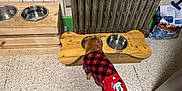 Chip is registered to the contest to win money with this photo: dog, puppy, sweater, plaid, mickey_mouse, feeding_station, wooden, metal_bowls, radiator, tiled_wall, floor, pet_food, bag, kitchen, indoor, brown_dog, small_dog, pet_care, cozy, home