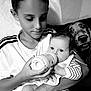 child, baby, feeding, bottle, dog, black_and_white, indoor, couch, striped_clothing, smiling_dog, family, portrait, tender_moment, holding, young_child, infant, human, pet, caregiving, closeup