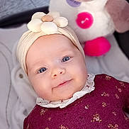 Lucie a rejoint le concours — aidez-le/la à gagner de superbes lots ! baby, infant, smile, headband, flower_headband, blue_eyes, plush_toy, stuffed_animal, musical_button, maroon_dress, patterned_clothing, hand, stroller_mesh, blanket, soft_texture, portrait, rosy_cheeks, cute, indoors, child