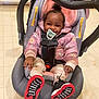 baby, child, car_seat, pacifier, smile, pink_jacket, black_shoes, red_sole, indoor, tiled_floor, cute, happy, infant, clothing, person, sitting, face, hair, hooded_jacket, safety_harness