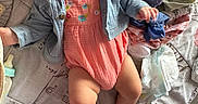 Alyssa is registered to the contest to win money with this photo: baby, baby_clothes, bedspread, bottle, bow, child, chubby_legs, clothing, curious, cute, denim_jacket, diaper, expression, headband, indoor, infant, laying_down, patterned, person, soft_lighting