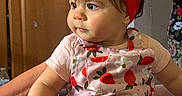Alyssa is registered to the contest to win money with this photo: toddler, child, red_bow, headband, strawberry_pattern, pink_clothing, indoor, person, curious, wide_eyes, soft_cheeks, sitting, arm_support, background_person, floral_pants, natural_light, portrait, baby, cute, casual