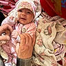 Alyssa is registered to the contest to win money with this photo: baby, infant, pink_pajamas, floral_hat, blanket, hand, adult_hand, plaid_shirt, cozy, soft_toys, smiling, cute, child, person, indoors, comfort, warm, fabric, pattern, toddler