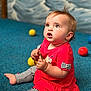 baby, blue_ball, blue_carpet, bracelet, casual_clothing, child, curious_expression, cute, floor, indoor, orange_ball, person, play, portrait, red_dress, sitting, striped_leggings, toy, yellow_ball, young_child