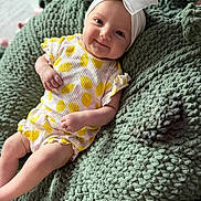 Emma joined the competition — help win amazing prizes! baby, infant, smile, headband, bow, yellow_clothing, white_clothing, knit_blanket, green_blanket, texture, cute, happy, indoors, child, person, portrait, sitting, cozy, soft, young