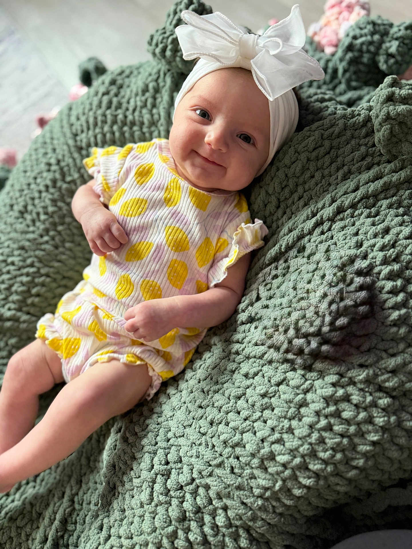 Emma joined the competition — help win amazing prizes! baby, infant, smile, headband, bow, yellow_clothing, white_clothing, knit_blanket, green_blanket, texture, cute, happy, indoors, child, person, portrait, sitting, cozy, soft, young
