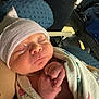 newborn, baby, sleeping, hospital_blanket, striped_cap, hand, person, phone, cushion, luggage, indoor, closeup, portrait, infant, cozy, resting, wrapped, skin, peaceful, family