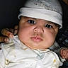 adult, baby, caregiver, child, close_up, clothing, curious, dim_lighting, eyes, face, flash_photography, hands, hat, indoor, infant, lying_down, onesie, pacifier_clip, portrait, white_hat