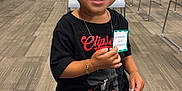 Indya is registered to the contest to win money with this photo: toddler, child, smiling, standing, indoor, carpet, jeans, sneakers, black_tshirt, bracelet, earrings, badge, office, chairs, door, exit_sign, cubicles, happy, person, hair_bun