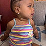 toddler, child, girl, indoors, sitting, romper, striped_clothing, earrings, hairstyle, top_bun, couch, blanket, home, cute, side_view, curious, baby, furniture, cozy, portrait