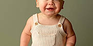 Briggs is registered to the contest to win money with this photo: baby, infant, smiling, portrait, studio, green_background, knitted_outfit, overalls, sitting, cute, chubby_cheeks, child, neutral_backdrop, high_key_lighting, single_subject, seated_pose, fashion, hand, legs, happy