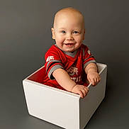 Briggs joined the competition — help win amazing prizes! baby, child, infant, smiling, white_box, red_shirt, portrait, studio, sitting, hands, face, bald_head, cheeks, grey_background, one_person, cute, happy, blue_eyes, indoor, studio_lighting