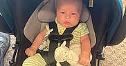 Atlas is registered to the contest to win money with this photo: baby, car_seat, infant, toy, pajamas, striped_clothing, blue_canopy, carrying, sitting, serious_face, child, indoor, safety_harness, floor, carpet, person, head, legs, feet, plush_toy