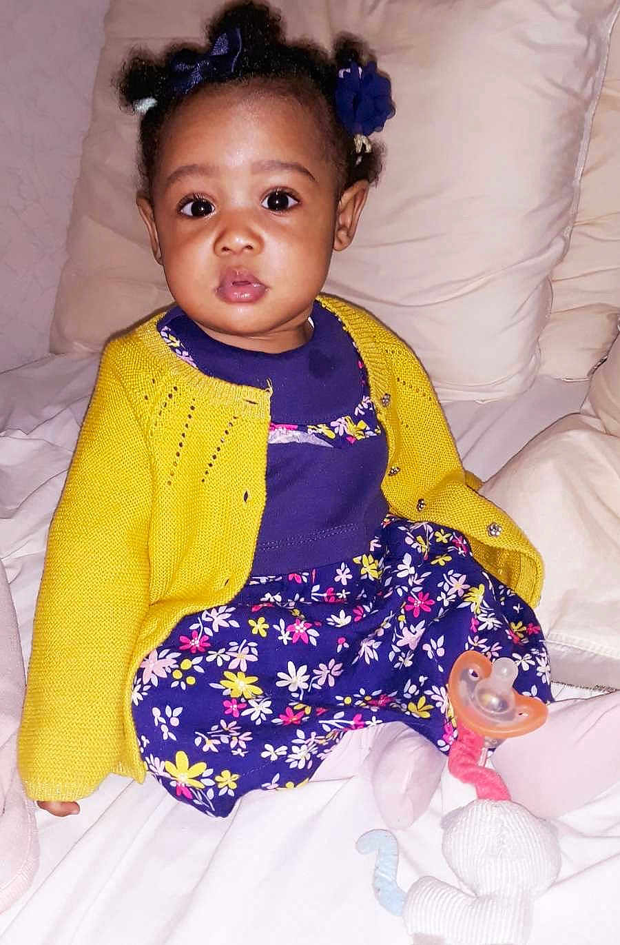 Marie-Sainte participe au concours pour gagner de l'argent avec cette photo : baby, child, girl, dress, yellow_cardigan, hair_bows, pacifier, plush_toy, bed, pillow, sitting, indoors, cute, portrait, clothing, infant, soft_toys, comfort, childhood, happy