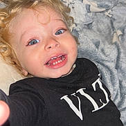 Kahyl a rejoint le concours — aidez-le/la à gagner de superbes lots ! child, toddler, smiling, curly_hair, blue_eyes, black_shirt, blanket, indoor, cute, happy, person, face, expression, closeup, portrait, baby, young_child, cozy, soft_texture, playful