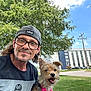 building, cap, casual, daylight, dog, glasses, grass, happy, leash, man, nature, outdoor, person, pet, portrait, sidewalk, sky, smile, tree, urban