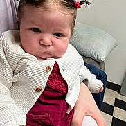 Ana a rejoint le concours — aidez-le/la à gagner de superbes lots ! baby, burgundy_outfit, child, clothing, cozy, cute, expression, face, floor_tiles, hand, holding, indoor, knitwear, person, pigtails, pillow, portrait, sitting, white_cardigan, young