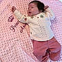 baby, infant, blanket, pink, clothing, sweater, pants, face, person, cute, lying_down, embroidery, soft_texture, happy, newborn, child, portrait, indoor, warm, cozy